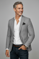 Man wearing a gray blazer over a white shirt with blue jeans on a gray background