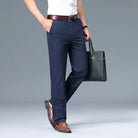 Person wearing navy pants with a white shirt, brown belt, and brown shoes, holding a black briefcase on a gray background.