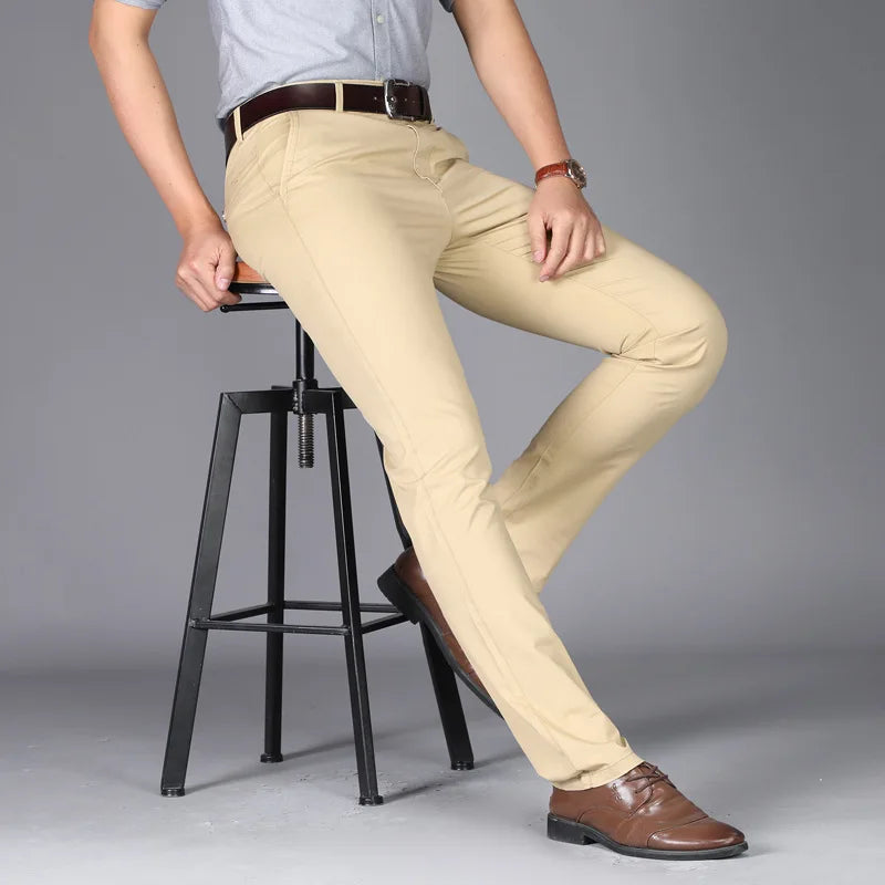 Person wearing beige pants and brown shoes sitting on a black stool against a gray background