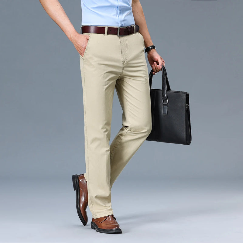 Person wearing beige pants and brown shoes holding a black briefcase on a gray background