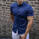 Man wearing a blue short-sleeve shirt against a brick wall