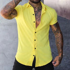 Person wearing a yellow sleeveless shirt with tattoos on arms against a gray background