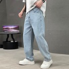Person wearing light blue jeans and white sneakers in a minimalistic setting with a gray background.