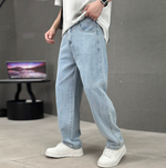 Person wearing light blue jeans and white sneakers in a minimalistic setting with a gray background.