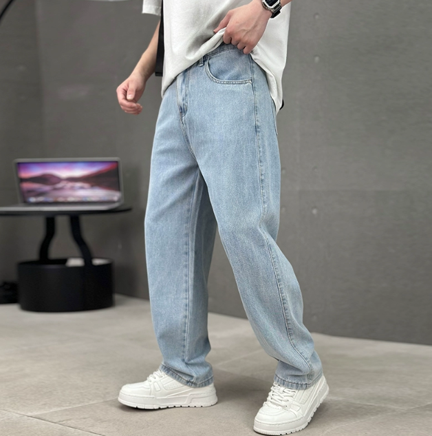 Person wearing light blue jeans and white sneakers in a minimalistic setting with a gray background.