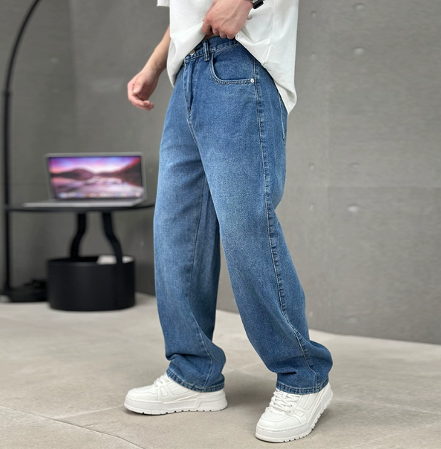 Person wearing blue jeans and white sneakers in a minimal indoor setting