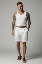Person wearing white shorts and a white shirt with tattoos on arms, holding a bottle.