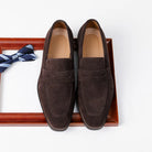 Pair of brown suede loafers on a white background with a striped tie.