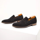 Pair of black suede loafers with wooden accents on a white background