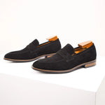 Pair of black suede loafers with wooden accents on a white background