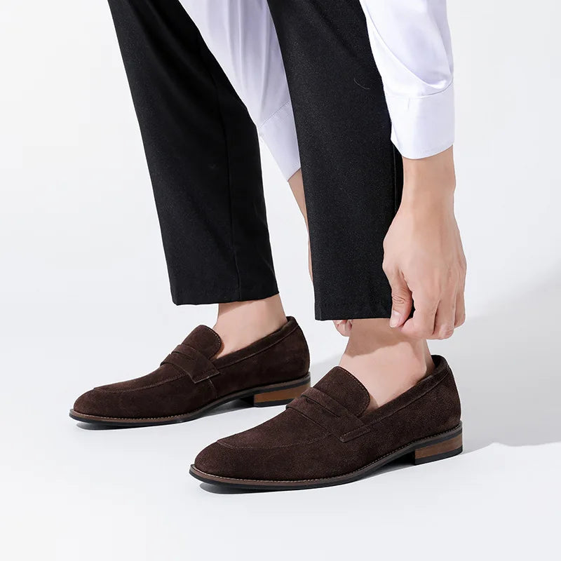 Brown loafers worn with black pants and a white shirt on a light gray background