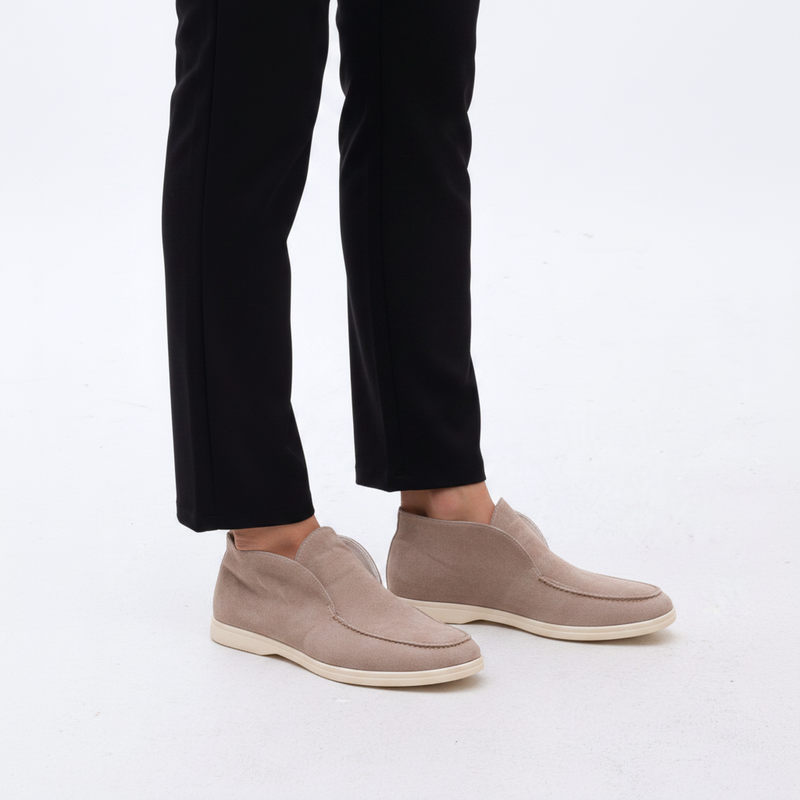 Beige slip-on shoes worn with black pants on a light background