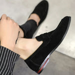 Black loafers worn with a striped sock on a neutral background