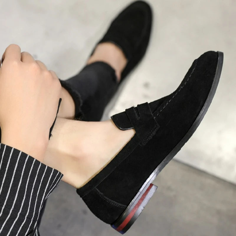 Black loafers worn with a striped sock on a neutral background
