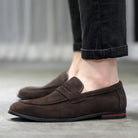 Brown loafers worn with dark jeans on a neutral background