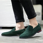 Green loafers worn with black pants on a neutral background