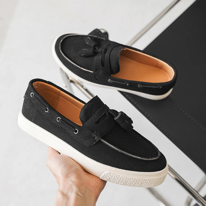 Black loafers with white soles held by a hand on a light background