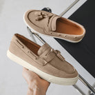 Pair of beige loafers with tassels held by a hand on a light gray background