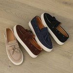 Four pairs of loafers in beige, brown, navy, and black on a wooden floor.