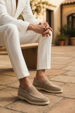 Person wearing beige loafers and white pants sitting on a wooden bench.
