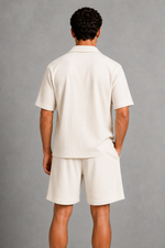Person wearing a beige outfit with a shirt and shorts on a gray background