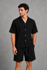 Man wearing a black button-up shirt and shorts against a gray background