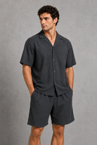 Man wearing a dark gray shirt and shorts against a gray background