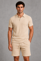 Man wearing a beige polo shirt and shorts against a gray background