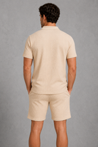 Man wearing a beige polo shirt and shorts against a gray background