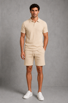 Man wearing a beige polo shirt and shorts set against a gray background
