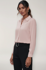 Person wearing a light pink blouse and black pants against a white background