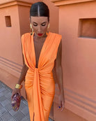 Woman in an orange dress standing against a peach-colored wall.