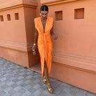Woman in an orange dress standing against a terracotta wall.