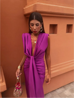 Woman in a vibrant purple dress standing against an orange wall.