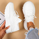 White sneakers being held by a hand with a beige background