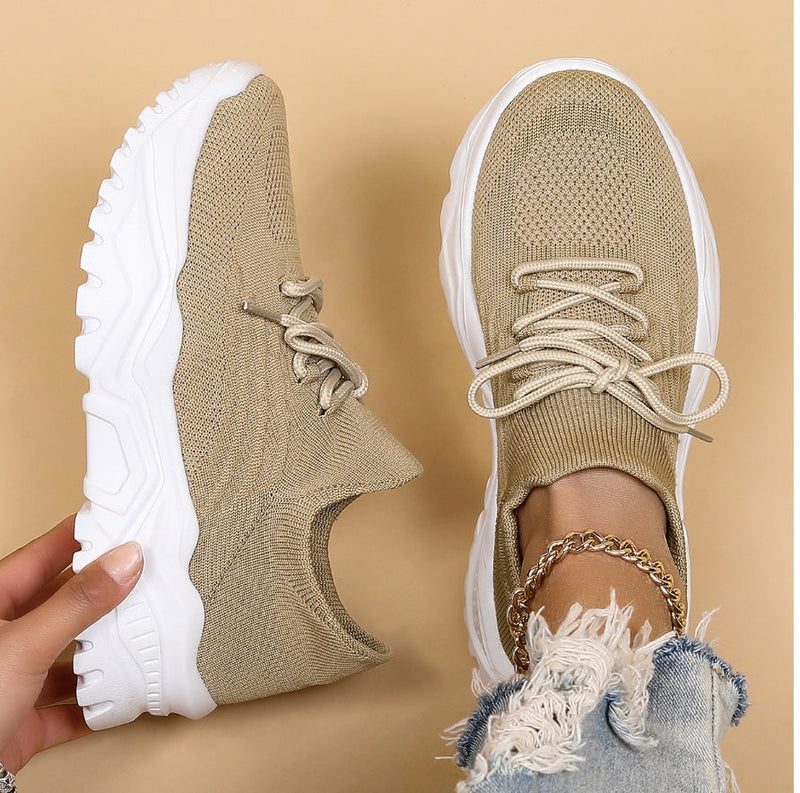 Beige sneakers with white soles worn by a person on a beige background