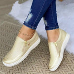 Gold slip-on sneakers worn with blue jeans on a textured surface.