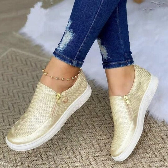 Gold slip-on sneakers worn with blue jeans on a textured surface.