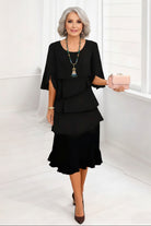 Woman wearing a black dress with ruffled layers, holding a pink clutch against a white background