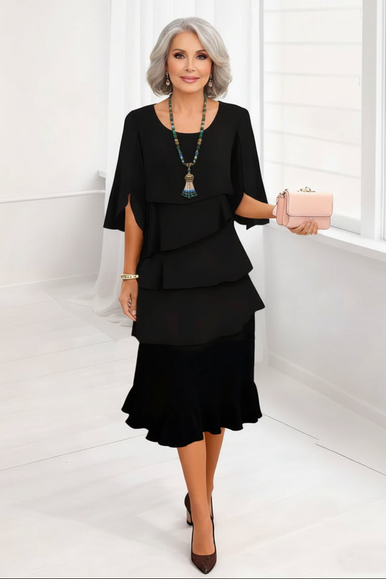 Woman wearing a black dress with ruffled layers, holding a pink clutch against a white background