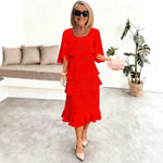 Woman in a red dress holding a pink clutch in a modern living room.
