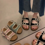 Two pairs of embellished sandals on feet with jeans, one black and silver, one multicolor.