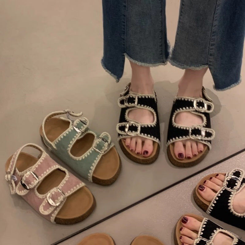 Two pairs of embellished sandals on feet with jeans, one black and silver, one multicolor.