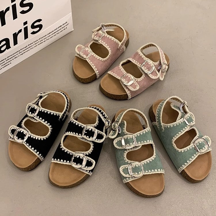 Four pairs of children's sandals in different colors on a gray surface.