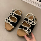 Black sandals with white lace details on a beige surface