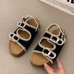 Black sandals with white lace details on a beige surface