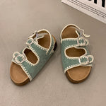 Pair of green sandals with white straps on a gray surface
