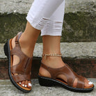Brown sandals worn with white pants against a concrete background