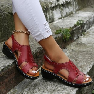 Red sandals worn on feet with white pants sitting on stone steps.