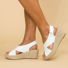 White wedge sandals with jute sole worn by a person on a beige background